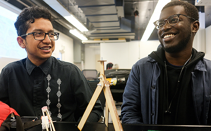 Two male students smiling and working on a project