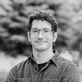 Headshot of Devon Ward, designer, artist, and educator, with curly black hair, glasses, and a button‑down collared shirt, looking thoughtfully toward the camera.