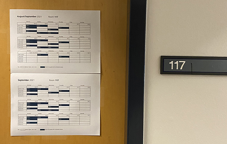 Door with schedule fixed to it next to sign with numbers 117