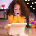 Image of a little girl showing surprise from the content of a box. The content is not visible but it seems to be a Christmas gift.