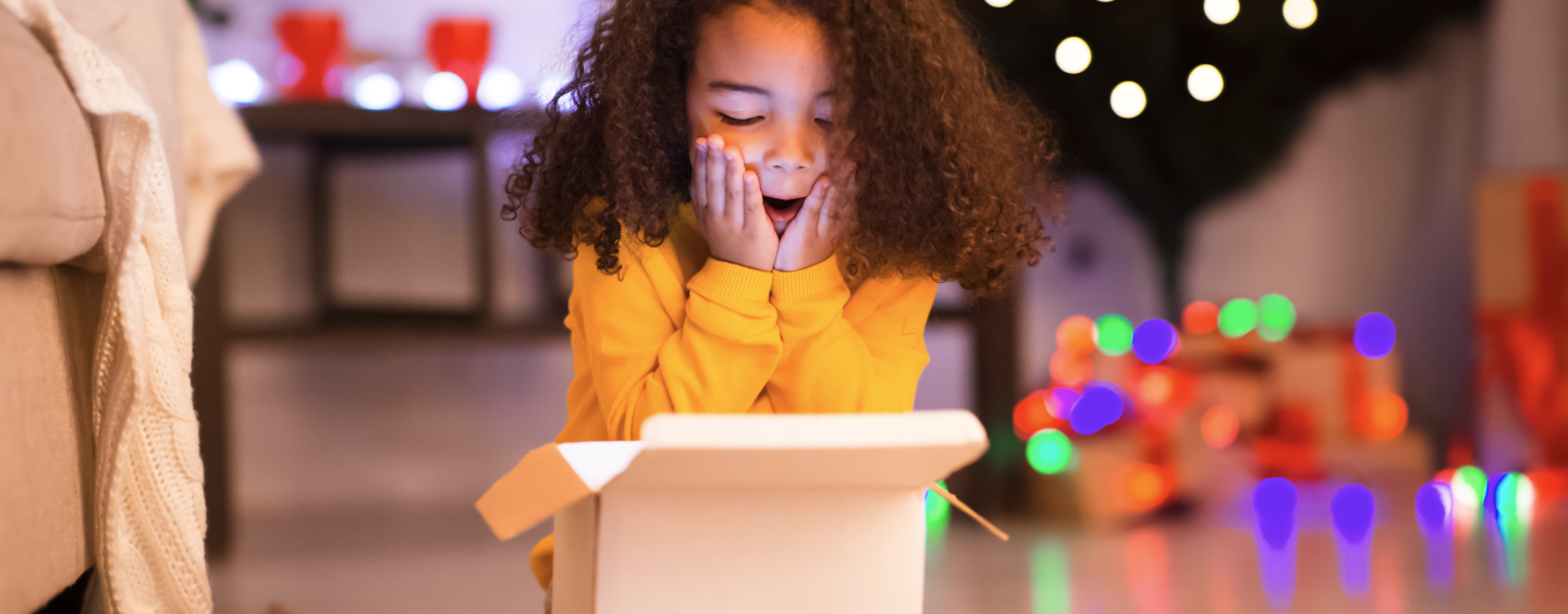 Image of a little girl showing surprise from the content of a box. The content is not visible but it seems to be a Christmas gift.