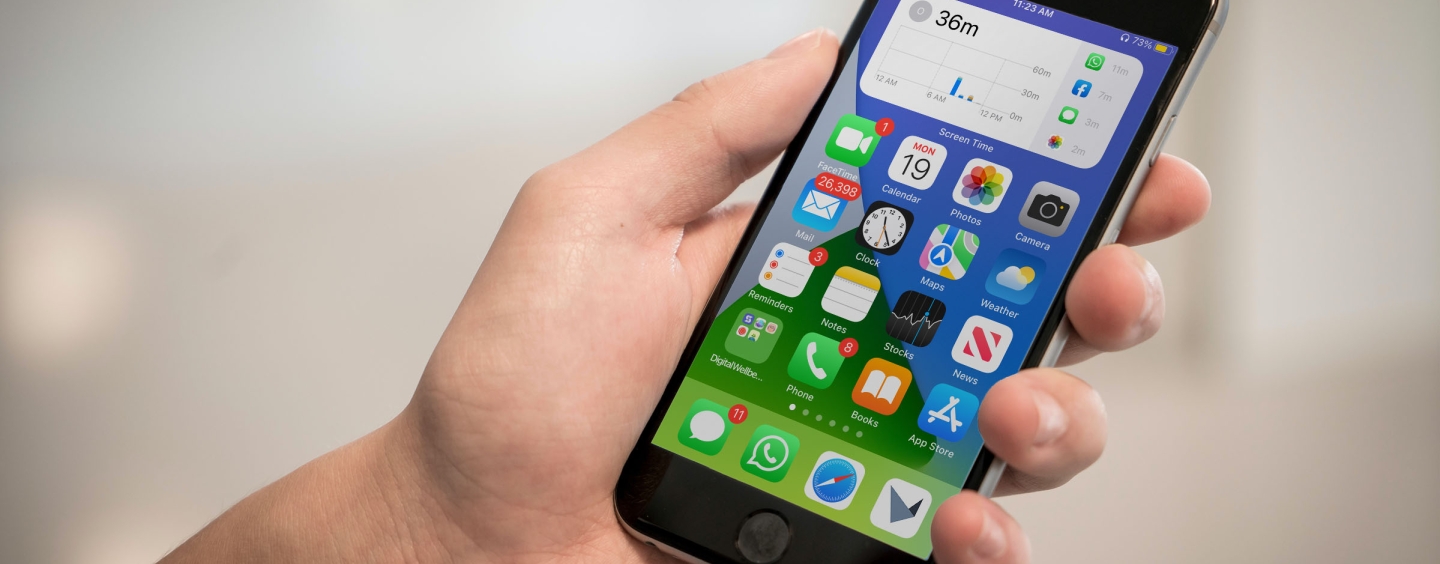 Hand holding an iPhone whose screen shows the home screen, including the iOS screen time widget