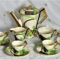 A coffee set with a coffee pot and four coffee cups with saucers. All objects have an ivory, cream white color as a base and some decoration in the form of swoshes in green and gold color. 